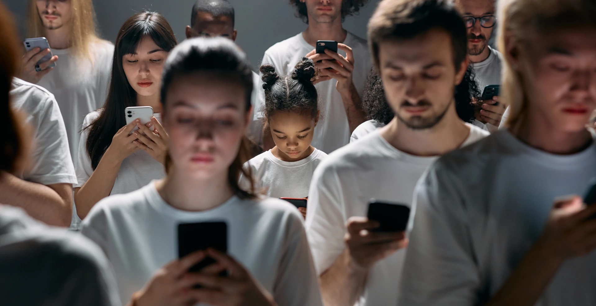 A crowd of people with white shirts facing the viewer. Everyone stared on their smartphone.